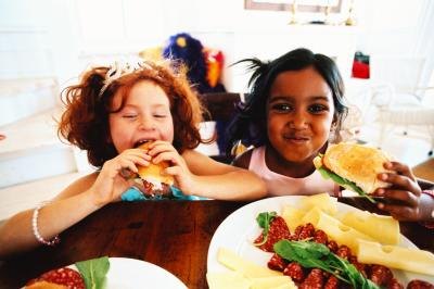 Two girls eat finger sandwiches.