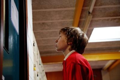 A school boy stands outside of an administrator's office.