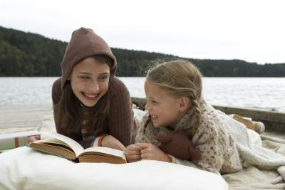 Children reading a book on a lakeside.