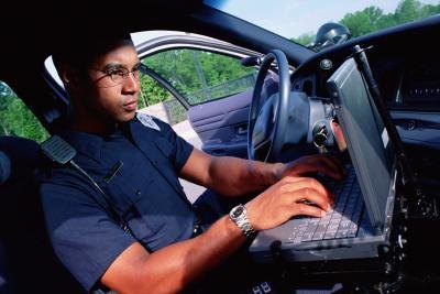 An officer works on a computer in a vehicle. An officer works on a computer in a vehicle.