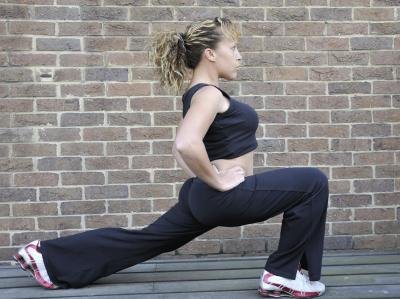 A woman performs a lunge while keeping her hands on her waist.