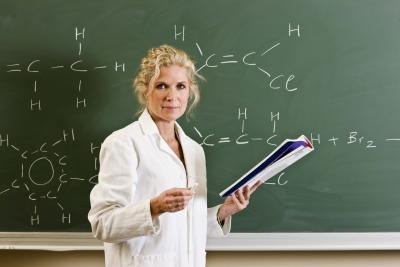 Female teacher holding book standing in front of blackboard.