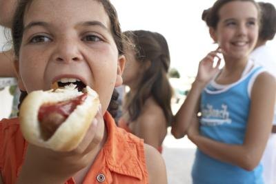 A girl takes a bite of a hot dog with ketchup.