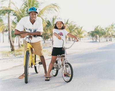 A dad and his daughter ride bikes together along the beach.