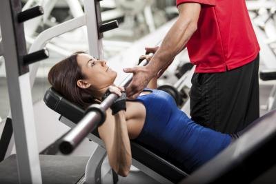 A woman does bench presses with the help of a trainer.