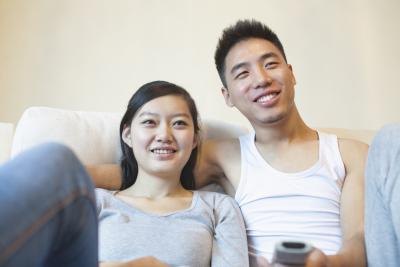A couple smiles while watching a movie together on the couch.
