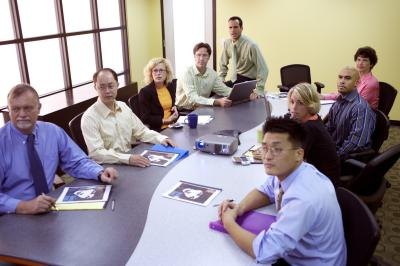 Employees sit at a curved table that divides into two in a conference room.