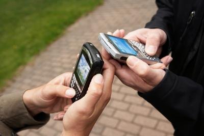 two people holding old cell phones two people holding old cell phones