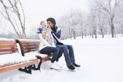 A couple is sitting on a park bench wearing ice skates.