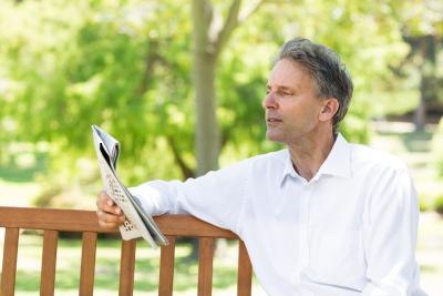Man reading a newspaper on a park bench