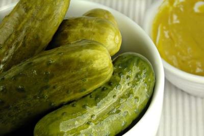 A close up of a small bowl of pickles next to a side of mustard