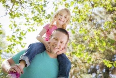 A little girl rides on her daddy's shoulders outside in the trees. A little girl rides on her daddy's shoulders outside in the trees.