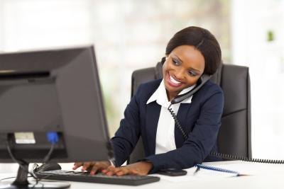 Young business woman on phone with client while researching on the computer.
