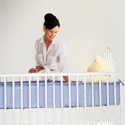 Young mother looking over a standard crib.