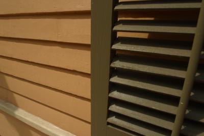 A close-up of the exterior of a home with tan siding and dark brown shutters.