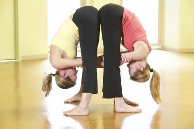 Two women do wide leg forward bend together at a studio.