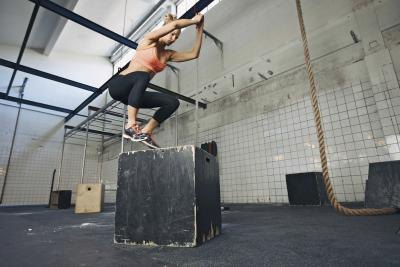 A woman performs plyometrics with a jump box.
