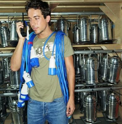 A man with a walkie-talking carries lighting equipment. A man with a walkie-talking carries lighting equipment.