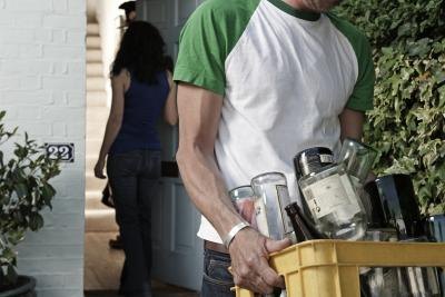A man carries alcohol bottles in a recycling bin to the curb. A man carries alcohol bottles in a recycling bin to the curb.