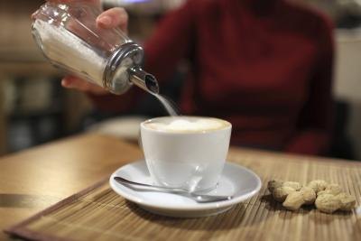 A woman pouring white sugar into a cup of coffee. A woman pouring white sugar into a cup of coffee.