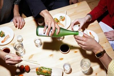 An overhead view of people enjoying sushi and sake at a table. An overhead view of people enjoying sushi and sake at a table.