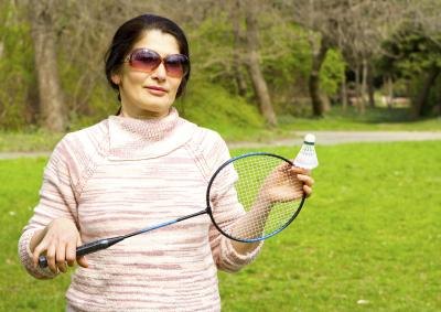 A woman holds a badminton racket and shuttle outside. A woman holds a badminton racket and shuttle outside.