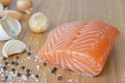 A fresh filet of chum salmon on a cutting board with shallots, garlic, sea salt and peppercorns. A fresh filet of chum salmon on a cutting board with shallots, garlic, sea salt and peppercorns.