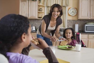 Mother feeding daughters breakfast at table Mother feeding daughters breakfast at table
