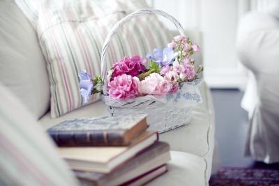A basket of flowers on a white sofa beside a stack of vintage books. A basket of flowers on a white sofa beside a stack of vintage books.