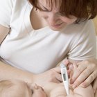 Close-up of a young man holding a digital thermometer with his son sitting on the bed behind him