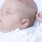 Baby smiling in bed with eyes closed and arms out.