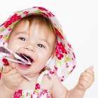 Baby girl (15-18 months) sitting on bed, biting toy