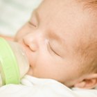 Söt bebis med mjölkflaska som sitter på sängen