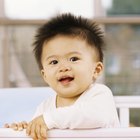 Baby smiling in bed with eyes closed and arms out.