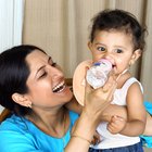 Cute baby with milk bottle sitting on bed