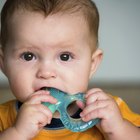 Baby girl (15-18 months) sitting on bed, biting toy