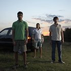 Three men sitting on wet sand by surfboards, rear view