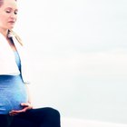 Pregnant woman drinking glass of water in kitchen at home.