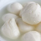 Small mozzarella balls in a white dish with liquid.