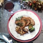 Pork chop in a serving dish with rosemary and tomatoes