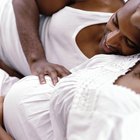 Beautiful pregnant woman sitting at bed and holds hands on belly in bedroom at home.
