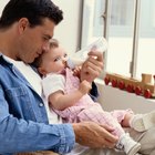 Süßes Baby mit Milchflasche auf dem Bett sitzend