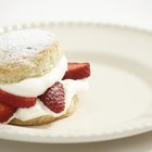 Scone and strawberry jam and clotted cream on a plate on a table with a red and white checkered table cloth