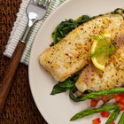 raw sliced steak of sturgeon fish with greens, lemon,