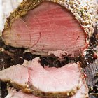 Slices of medium-rare roast beef shingled on a white plate with a side of fresh cherry tomatoes.