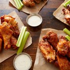 Baked chicken wings with sesame seeds and sweet chili sauce on white wooden board.