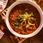 Beef chili with beans and cheese topping in a bowl on a table