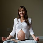Pregnant woman with cramping and lower back pain sitting on her bed