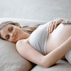 Beautiful pregnant woman holding her back while sitting on a bed