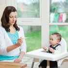 Close-up of a young man holding a digital thermometer with his son sitting on the bed behind him